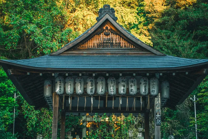 Wooden Shinto shrine among trees with hanging lanterns